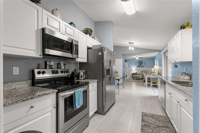 kitchen featuring stainless steel appliances, white cabinets, vaulted ceiling, a sink, and light stone countertops