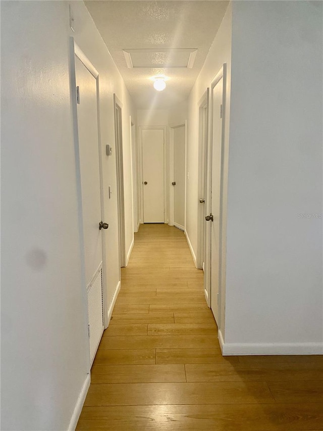 hallway with a textured ceiling and light hardwood / wood-style flooring