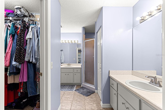 bathroom featuring tile patterned flooring, vanity, a shower with door, and a textured ceiling