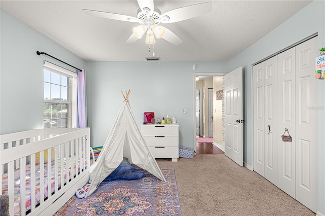 bedroom featuring ceiling fan, a textured ceiling, a closet, carpet, and a crib