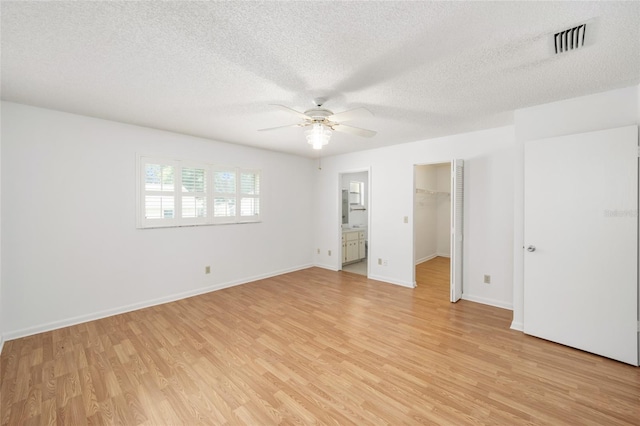 unfurnished bedroom featuring a spacious closet, ceiling fan, a textured ceiling, and light wood-type flooring