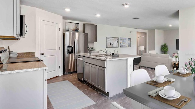 kitchen with appliances with stainless steel finishes, an island with sink, gray cabinetry, and sink