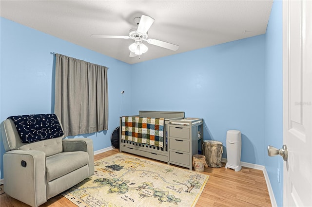 bedroom with a textured ceiling, ceiling fan, light hardwood / wood-style flooring, and a nursery area