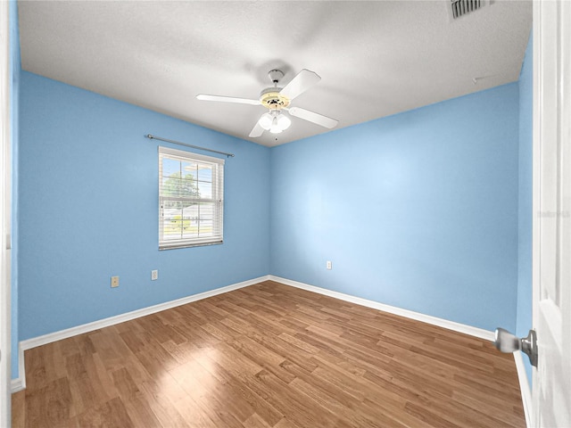 empty room with baseboards, a ceiling fan, wood finished floors, and visible vents