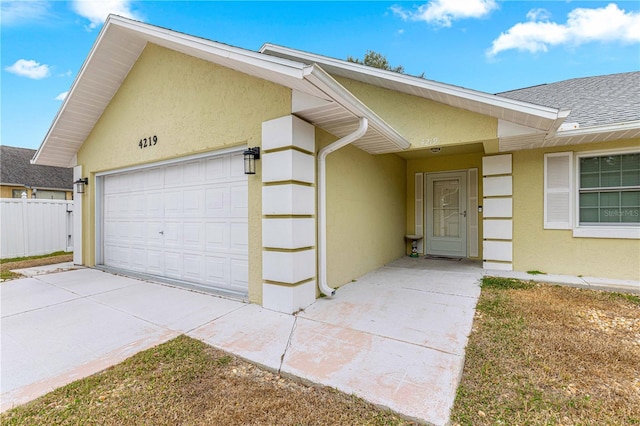 exterior space with a garage, stucco siding, fence, concrete driveway, and roof with shingles