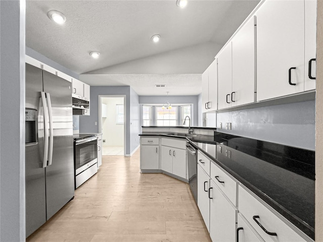 kitchen with appliances with stainless steel finishes, a sink, a peninsula, lofted ceiling, and light wood-style flooring