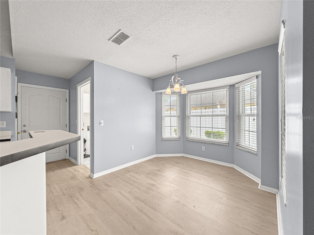 unfurnished dining area with a textured ceiling, visible vents, light wood-type flooring, baseboards, and an inviting chandelier