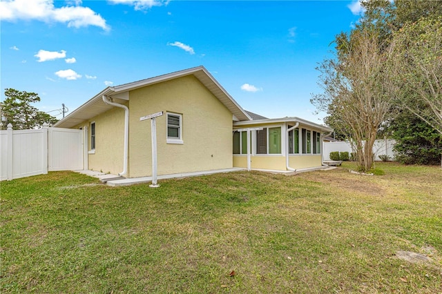 back of house with a lawn, fence, a sunroom, and stucco siding