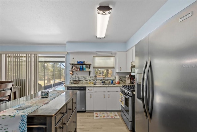 kitchen with light stone countertops, stainless steel appliances, sink, white cabinets, and light hardwood / wood-style floors