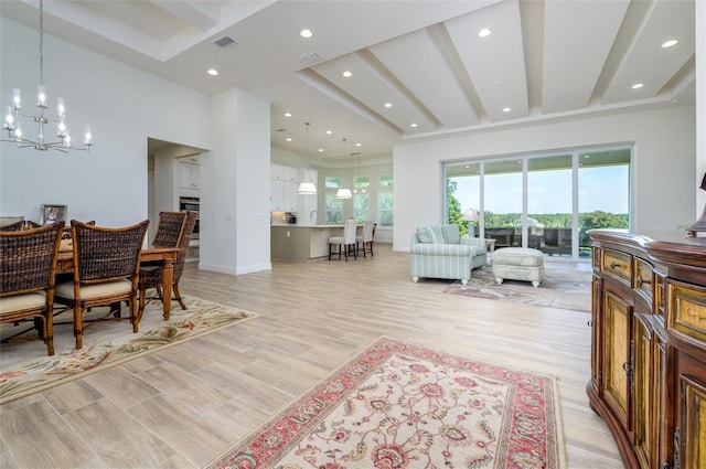 living room featuring a high ceiling, light wood-type flooring, a notable chandelier, and beam ceiling