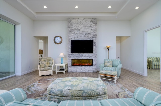 living room with a raised ceiling, a stone fireplace, and light hardwood / wood-style flooring