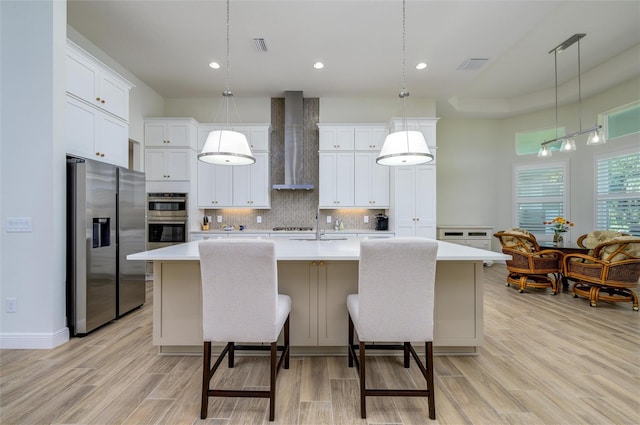 kitchen featuring pendant lighting, wall chimney range hood, stainless steel appliances, and a large island with sink