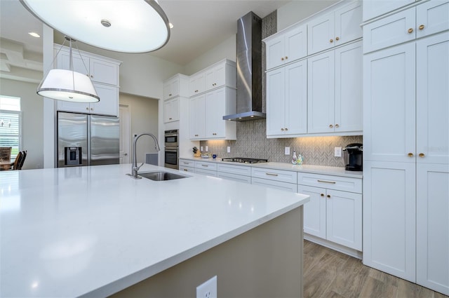 kitchen with appliances with stainless steel finishes, sink, white cabinetry, and wall chimney range hood