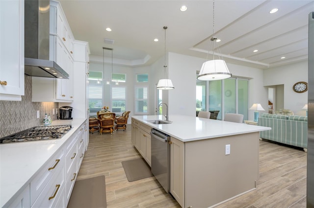 kitchen with sink, wall chimney range hood, light hardwood / wood-style floors, a center island with sink, and appliances with stainless steel finishes