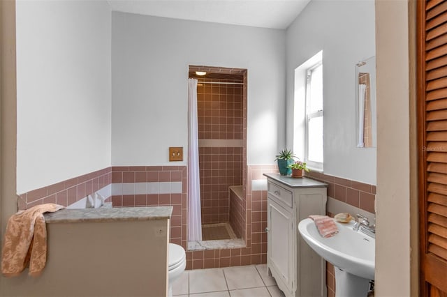 bathroom with tile patterned floors, sink, toilet, tiled shower, and tile walls