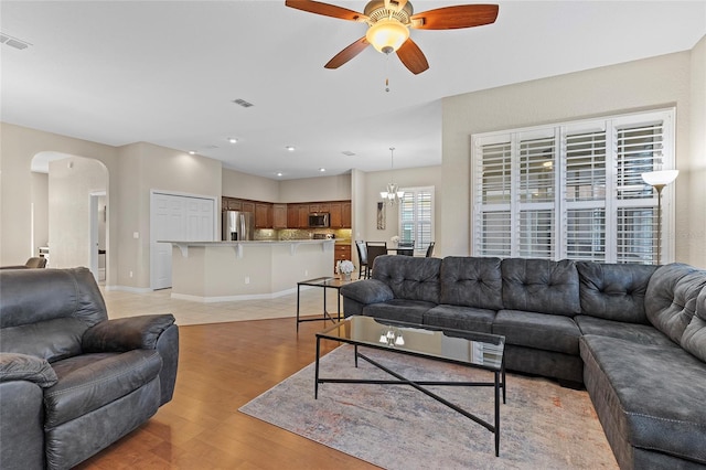 living room featuring ceiling fan with notable chandelier and light wood-type flooring