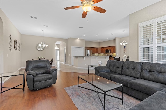 living room with ceiling fan with notable chandelier and light wood-type flooring