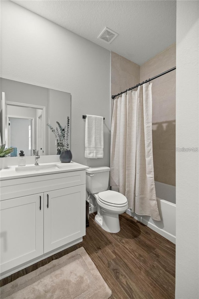 full bathroom with vanity, a textured ceiling, wood-type flooring, shower / bathtub combination with curtain, and toilet