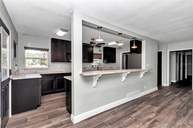 kitchen with pendant lighting, a textured ceiling, stainless steel refrigerator, ceiling fan, and a breakfast bar area