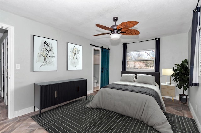 bedroom with ceiling fan, a barn door, a textured ceiling, dark parquet floors, and connected bathroom