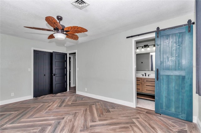 unfurnished bedroom with ceiling fan, sink, a barn door, a textured ceiling, and ensuite bath