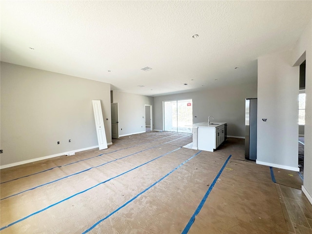 unfurnished living room with a sink, visible vents, baseboards, and a textured ceiling