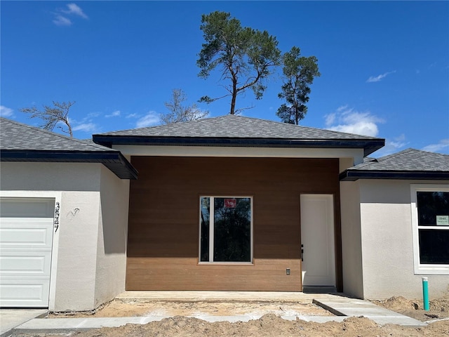 back of property with roof with shingles, an attached garage, and stucco siding