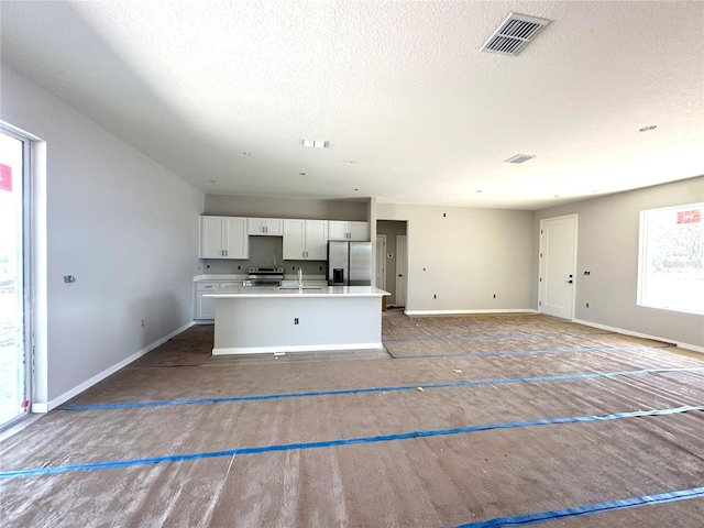 kitchen with stainless steel appliances, visible vents, baseboards, white cabinetry, and an island with sink