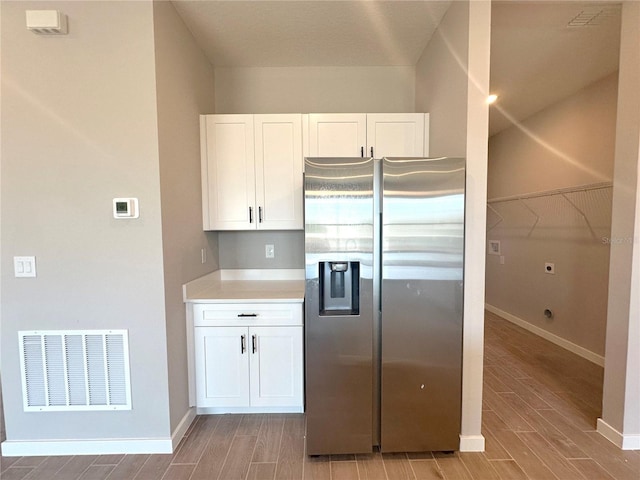 kitchen with wood finish floors, light countertops, visible vents, white cabinets, and stainless steel fridge with ice dispenser