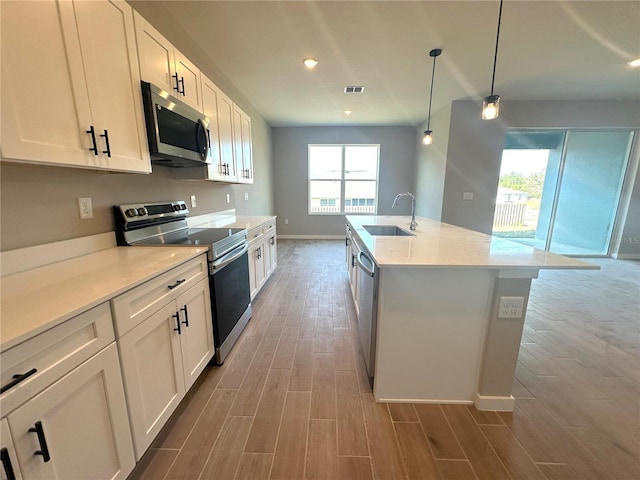 kitchen with appliances with stainless steel finishes, wood finished floors, light countertops, white cabinetry, and a sink