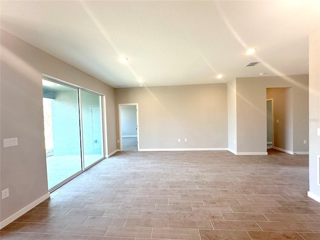 empty room featuring a textured ceiling, wood finished floors, visible vents, and baseboards