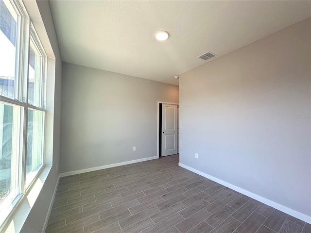 unfurnished room featuring dark wood-style floors, visible vents, and baseboards