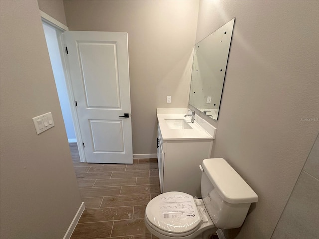 bathroom featuring toilet, wood tiled floor, vanity, and baseboards