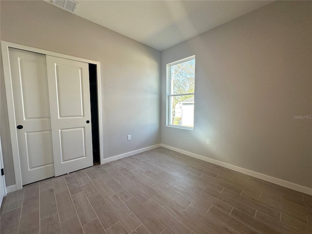 unfurnished bedroom featuring baseboards, a closet, visible vents, and wood finished floors