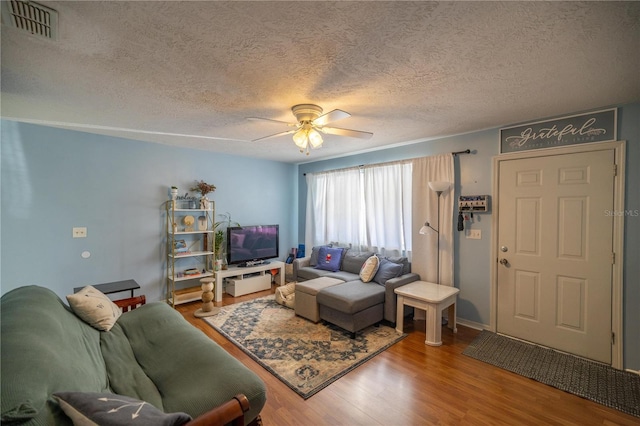 living room featuring hardwood / wood-style flooring, ceiling fan, and a textured ceiling