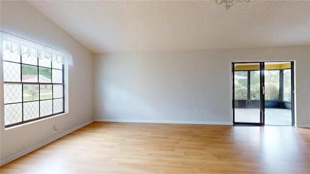 empty room featuring light hardwood / wood-style floors, lofted ceiling, a textured ceiling, and a wealth of natural light