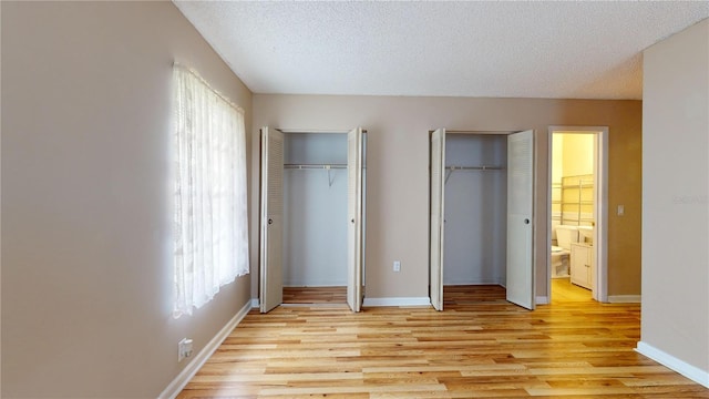 unfurnished bedroom featuring multiple closets, light hardwood / wood-style flooring, multiple windows, and a textured ceiling