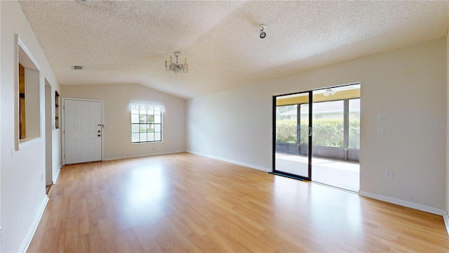 empty room featuring a notable chandelier, lofted ceiling, a textured ceiling, and light hardwood / wood-style flooring