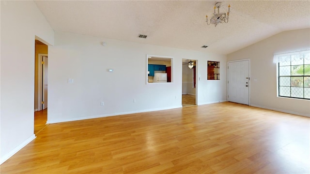 unfurnished room with light wood-type flooring, lofted ceiling, a textured ceiling, and an inviting chandelier