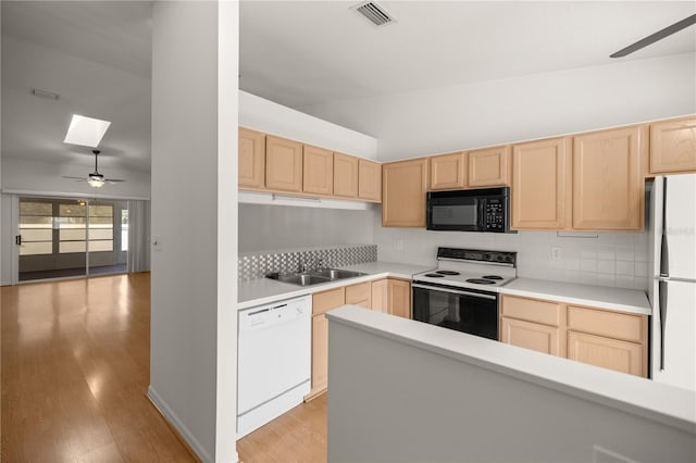 kitchen featuring vaulted ceiling with skylight, white appliances, and light brown cabinetry