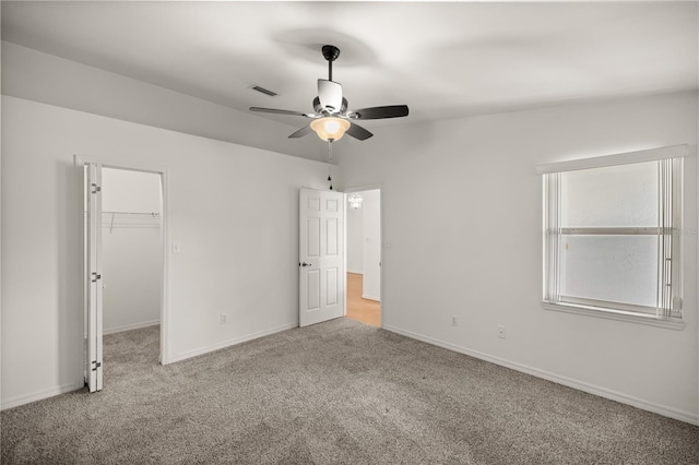 unfurnished bedroom featuring a spacious closet, a closet, ceiling fan, and light colored carpet