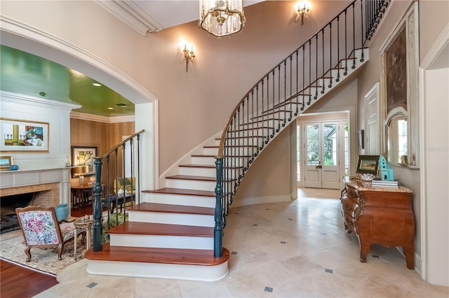 staircase featuring a tiled fireplace, an inviting chandelier, a high ceiling, and ornamental molding