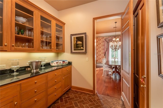 kitchen with dark stone counters, crown molding, pendant lighting, and a notable chandelier