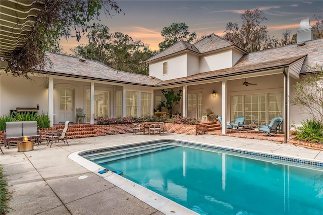 pool at dusk with ceiling fan and a patio