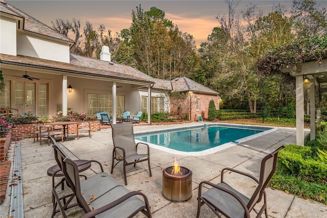 pool at dusk featuring a fire pit, ceiling fan, and a patio area