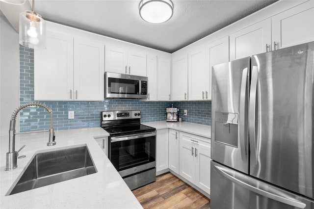 kitchen featuring white cabinetry, sink, light hardwood / wood-style flooring, decorative light fixtures, and appliances with stainless steel finishes