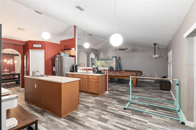 kitchen featuring hanging light fixtures, stainless steel refrigerator with ice dispenser, vaulted ceiling, a kitchen island with sink, and hardwood / wood-style flooring