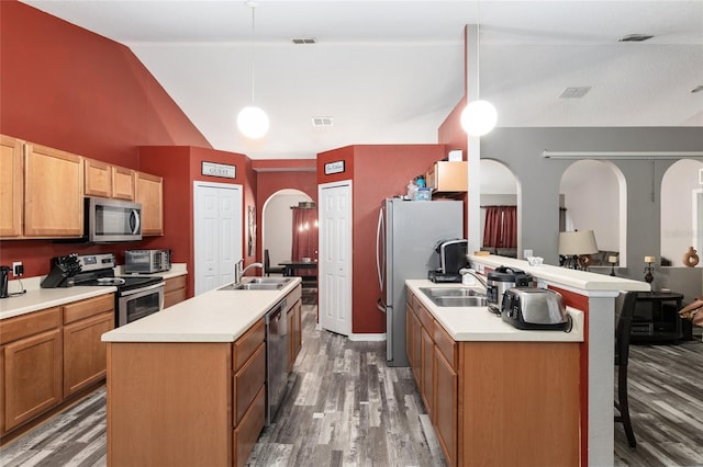 kitchen featuring appliances with stainless steel finishes, dark hardwood / wood-style flooring, decorative light fixtures, and a kitchen island with sink