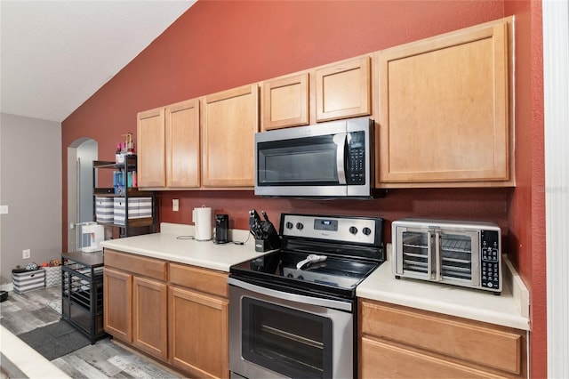 kitchen with light hardwood / wood-style floors, lofted ceiling, light brown cabinetry, and appliances with stainless steel finishes