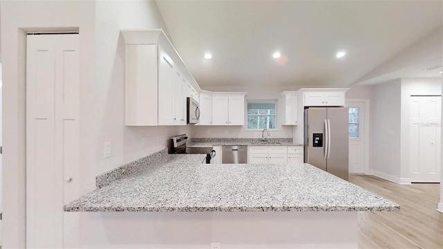 kitchen with kitchen peninsula, light stone counters, stainless steel appliances, light hardwood / wood-style flooring, and white cabinets